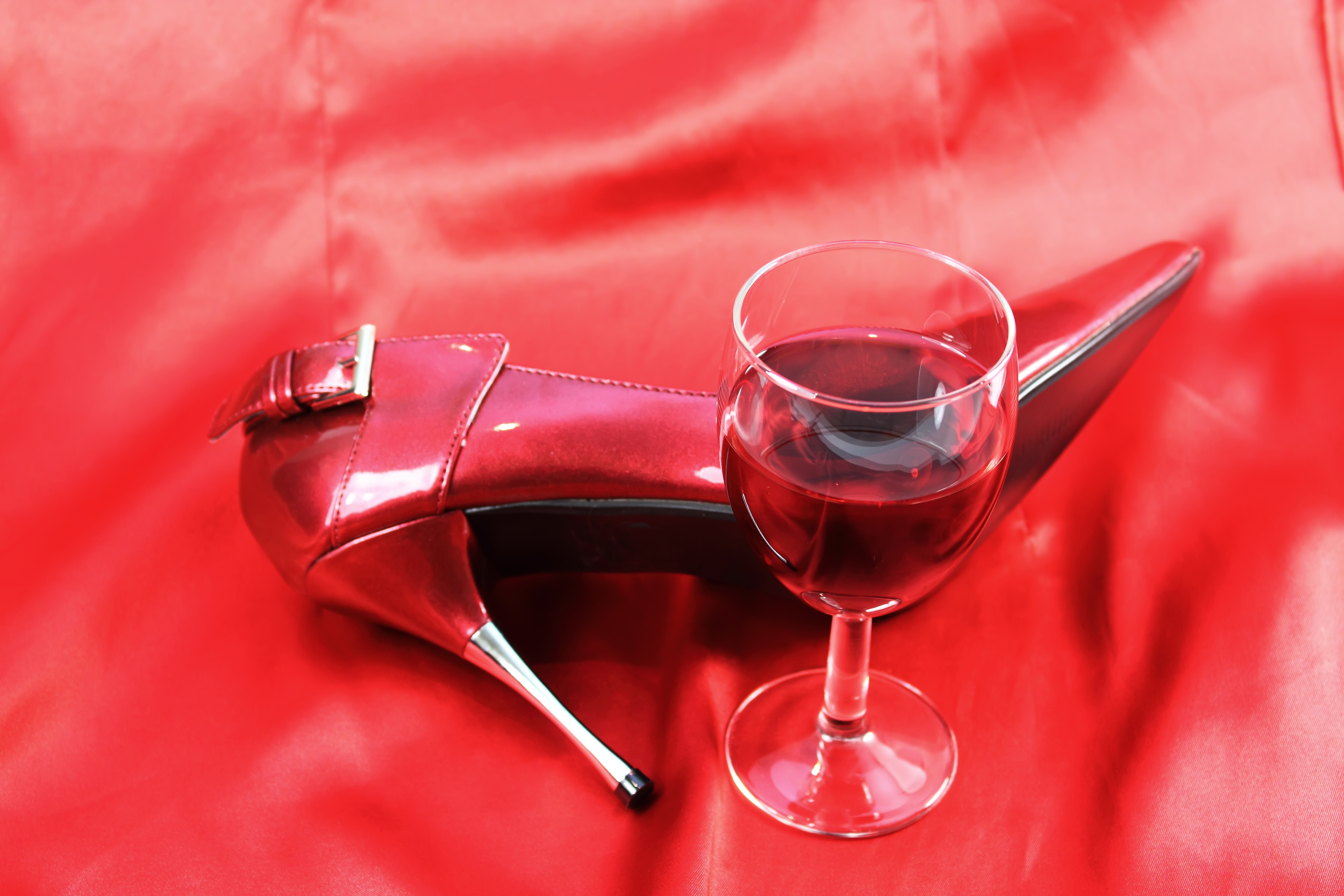 Red wine and heel on red satin background